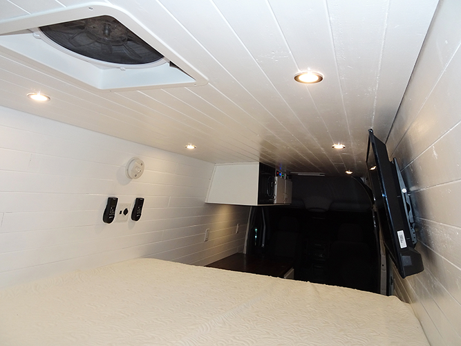 Bed of the Billy Goat camper van conversion with a slatted ceiling and marine-grade 12V electrical system.