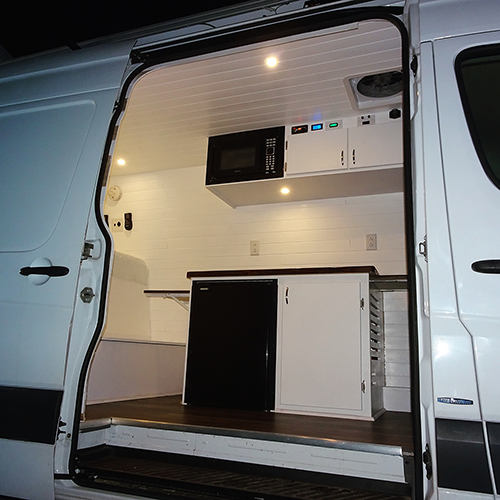 Interior of a finished camper van conversion with cabinetry, butcher block galley, and slatted ceiling